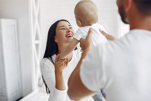 donna felice che guarda il suo bimbo, sorretto dal papà